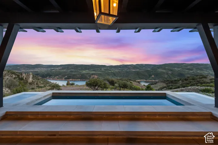 Integrated spa with surrounding stone coping, covered patio with exposed beam ceiling, and a prominent mountain and water backdrop