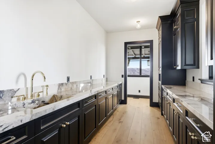 Hardwood flooring throughout, full-height dark wood cabinetry, light-toned stone countertops, integrated sink, and polished brass fixtures