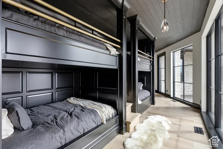 Built-in bunk beds with paneled construction, light wood-finish flooring, dark wood plank ceiling, and large windows with dark frames