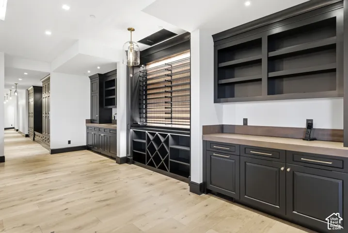 Light wood-finish flooring, dark cabinetry with hardware, built-in shelving, stone countertops, and recessed lighting