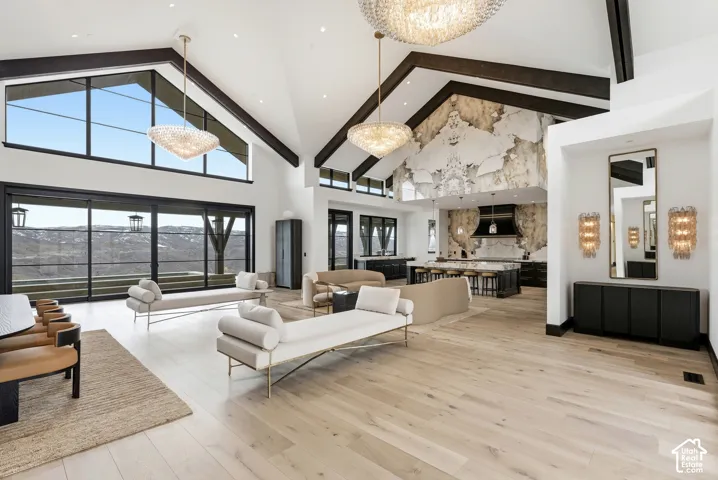 Vaulted ceilings with exposed dark wood beams, large format windows, light wood-finish flooring, and a stone accent wall