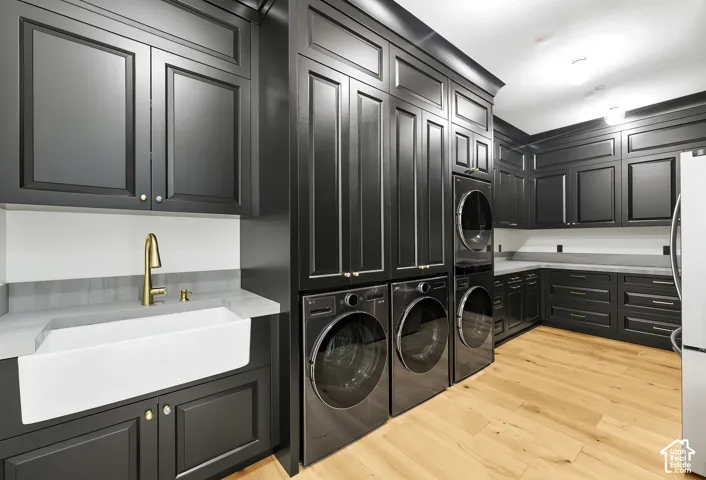 Extensive dark cabinetry with crown molding, light wood-finish flooring, white farmhouse sink with a brass-finish faucet, and light-toned countertops
