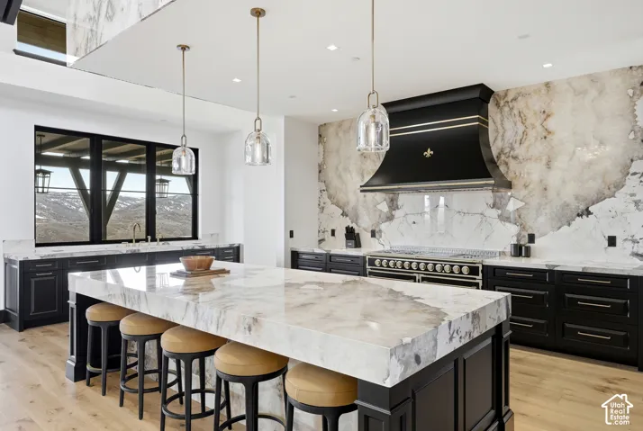 Gourmet kitchen with a large island, custom range hood, professional-grade range, dark cabinetry, and light wood-finish flooring