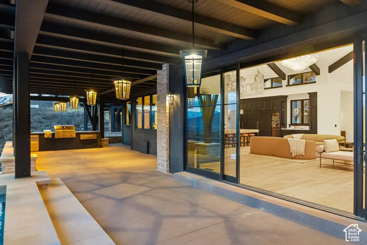 Covered patio with an outdoor kitchen featuring a built-in grill, multiple pendant light fixtures, wood-finish ceiling, and large sliding glass doors