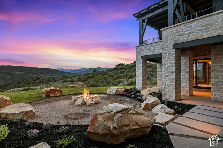 Stone exterior with a covered patio, upper-level balcony, and a dedicated fire pit area