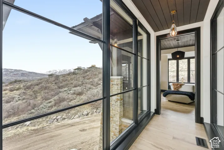 Expansive floor-to-ceiling windows, wood-finish flooring, dark wood-paneled ceiling, stone column, and a modern ceiling light fixture