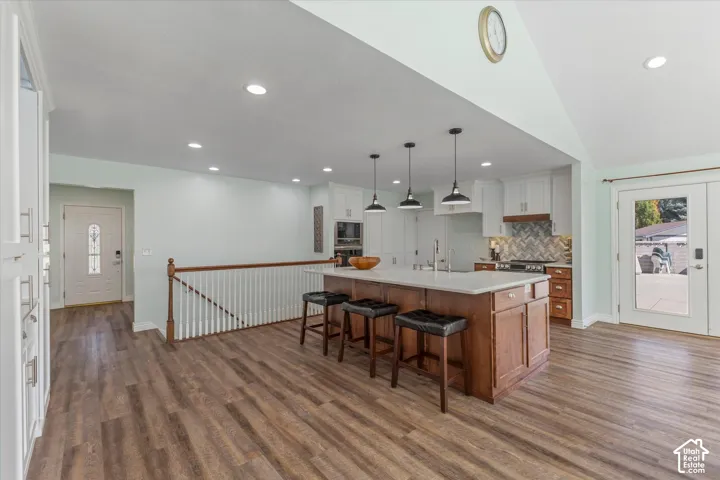 Spacious kitchen featuring an expansive island, white cabinetry, herringbone tile backsplash, and wood-finish flooring