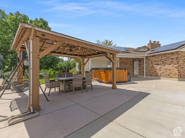 Expansive concrete patio with a wooden gazebo, an outdoor dining setup, and an outdoor spa