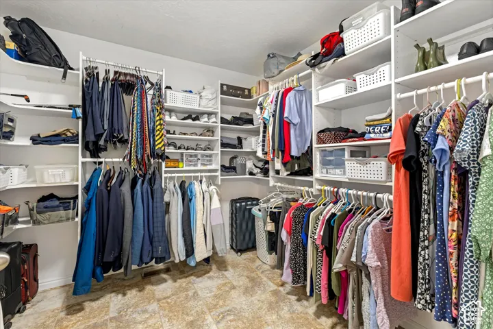 Expansive walk-in closet featuring built-in shelving, multiple hanging rods, and tile flooring