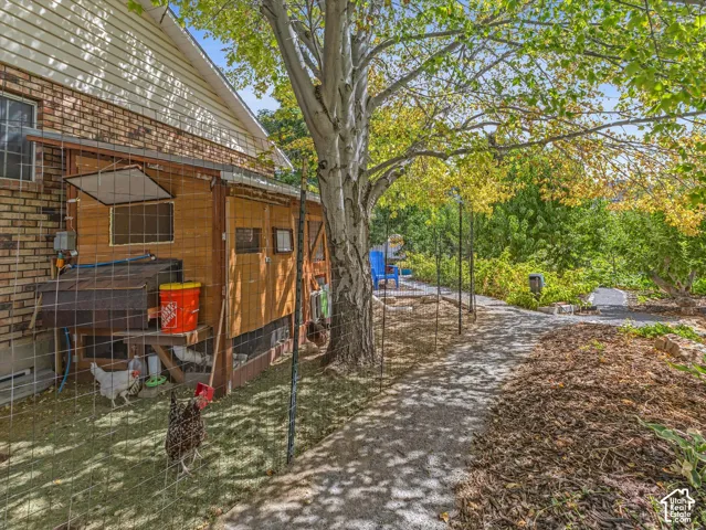 Exterior featuring a brick facade with horizontal siding, a built-in wood-sided coop, a paved pathway, and mature trees