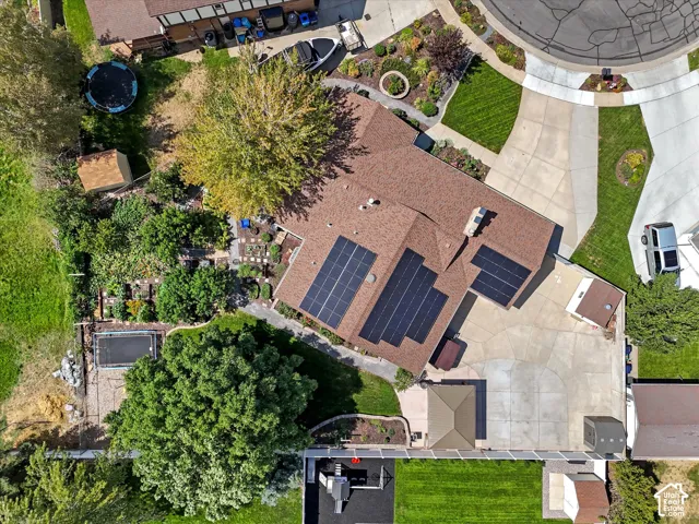 Extensive solar panel array, multi-level shingle roof, expansive concrete driveway, lush landscaping, and integrated garden beds