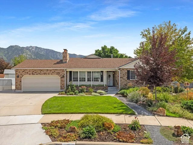 Brick and siding exterior with an attached garage, mature landscaping, and mountain backdrop