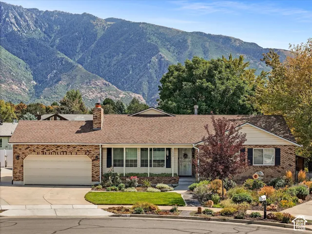 Brick exterior with a peaked roofline, attached garage, and mature front landscaping