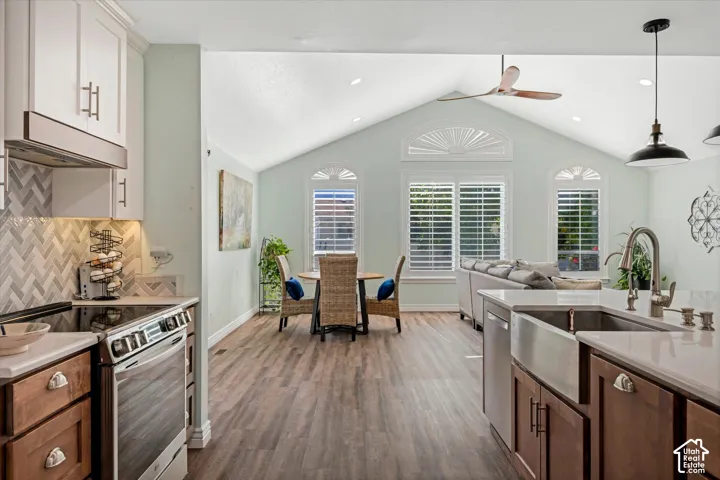Open-concept living area with vaulted ceiling, wood-finish flooring, and white plantation shutters