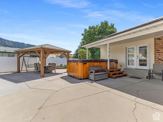 Expansive concrete patio featuring a wood-frame gazebo, a built-in spa, and a covered porch with double glass doors