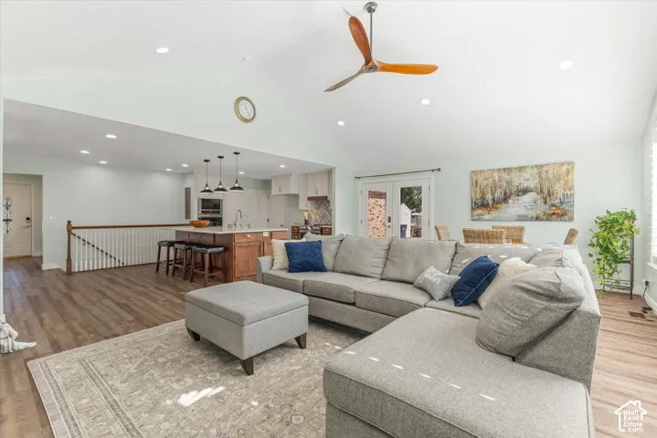 Vaulted ceiling with a wood-blade ceiling fan, wood-finish flooring, recessed lighting, white French doors, and a kitchen island with pendant lighting
