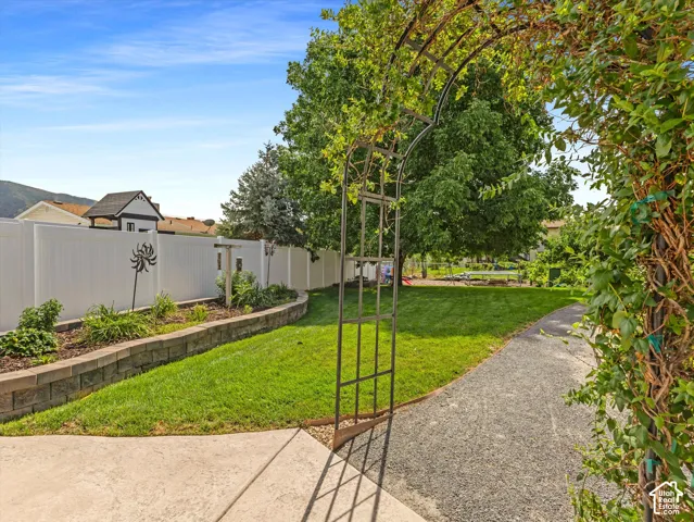 Expansive yard featuring a manicured lawn, gravel path, and a wrought iron archway with climbing foliage