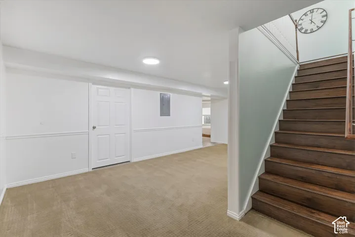 Plush carpeted flooring, white paneled wainscoting, recessed lighting, and wood-finish stairs with a white railing