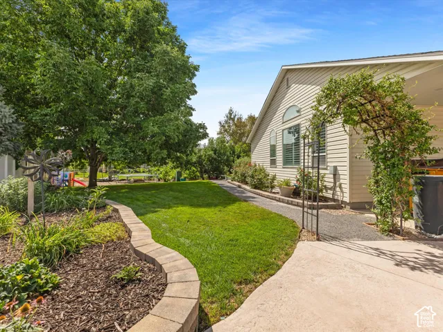 Expansive lawn area, established trees, concrete paver landscaping, and a side exterior featuring light-colored siding