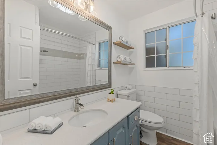 Quartz countertop vanity with blue cabinetry, framed mirror, wall-mounted light fixture, white subway tile shower, and wood-finish flooring
