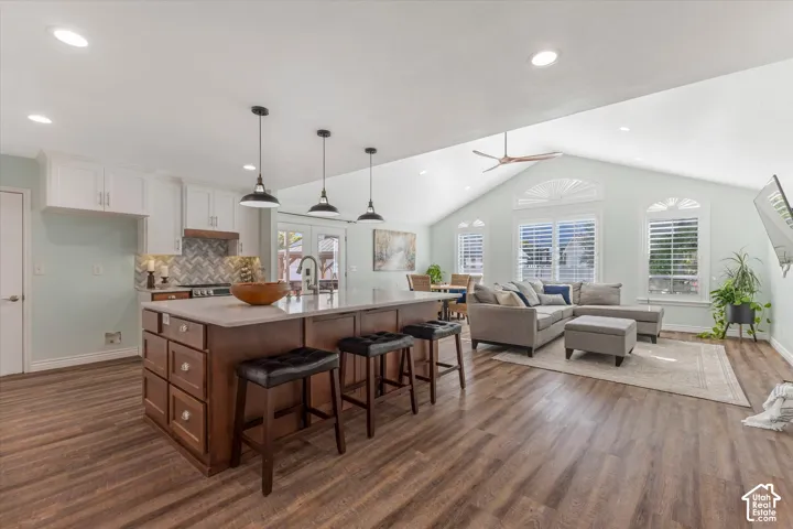 Vaulted ceiling with a ceiling fan, wood-finish flooring, kitchen island with seating, white shaker cabinetry, and French doors