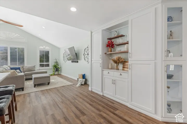 Vaulted ceilings, wood-finish flooring, white built-in cabinetry, arched windows with plantation shutters, and recessed lighting