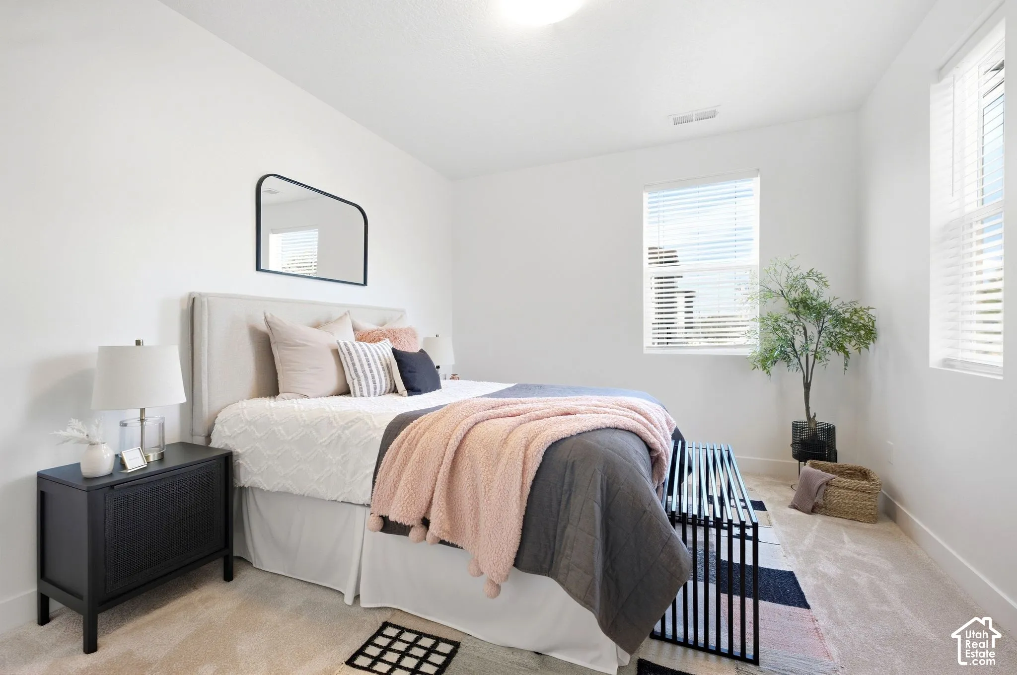 2nd bedroom.Bright bedroom featuring white walls, carpeted flooring, two windows with blinds, and an upholstered headboard