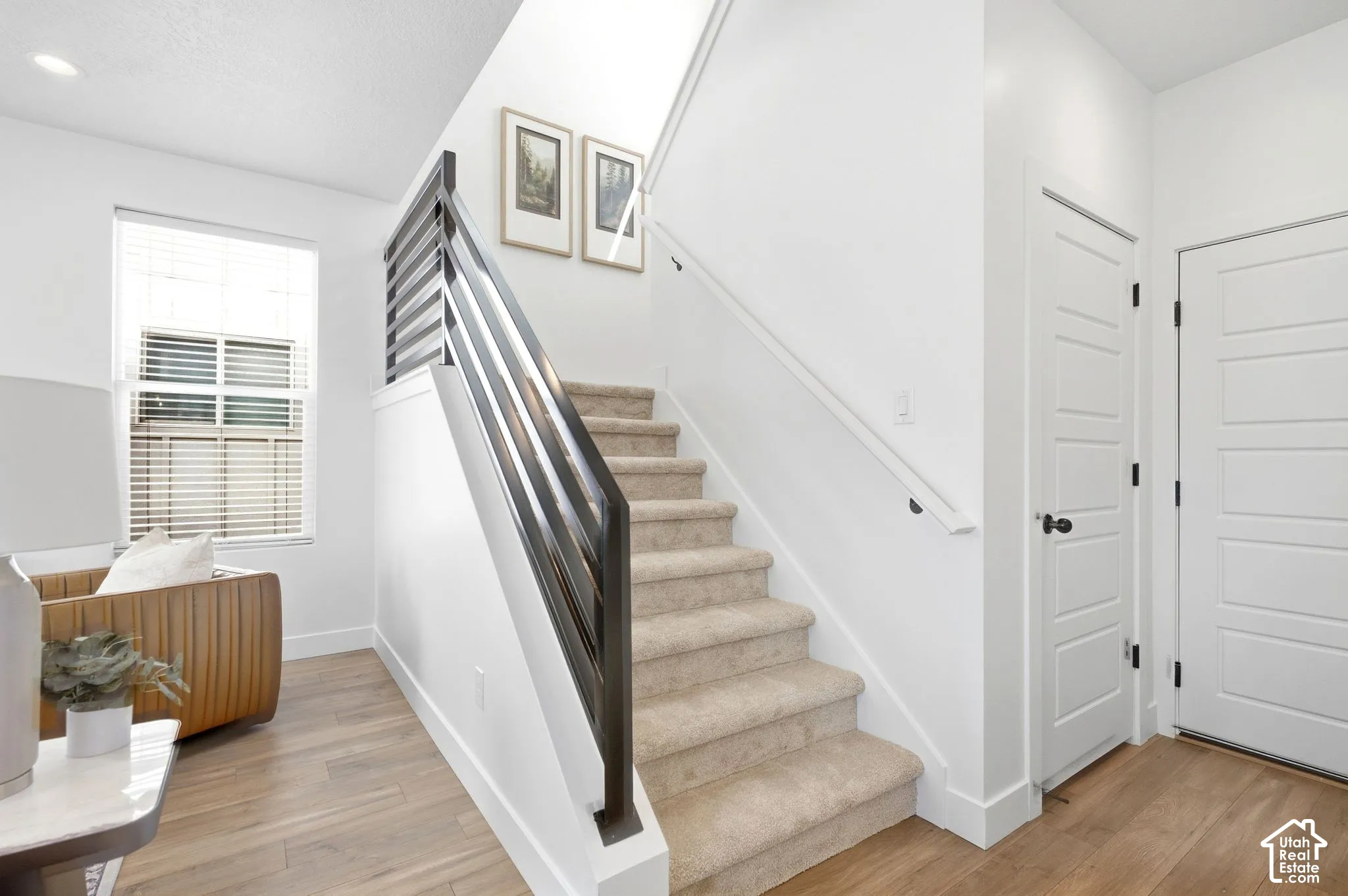 Modern stair railing with dark metal balusters, light wood-finish flooring, white paneled doors, and a neutral carpeted staircase
