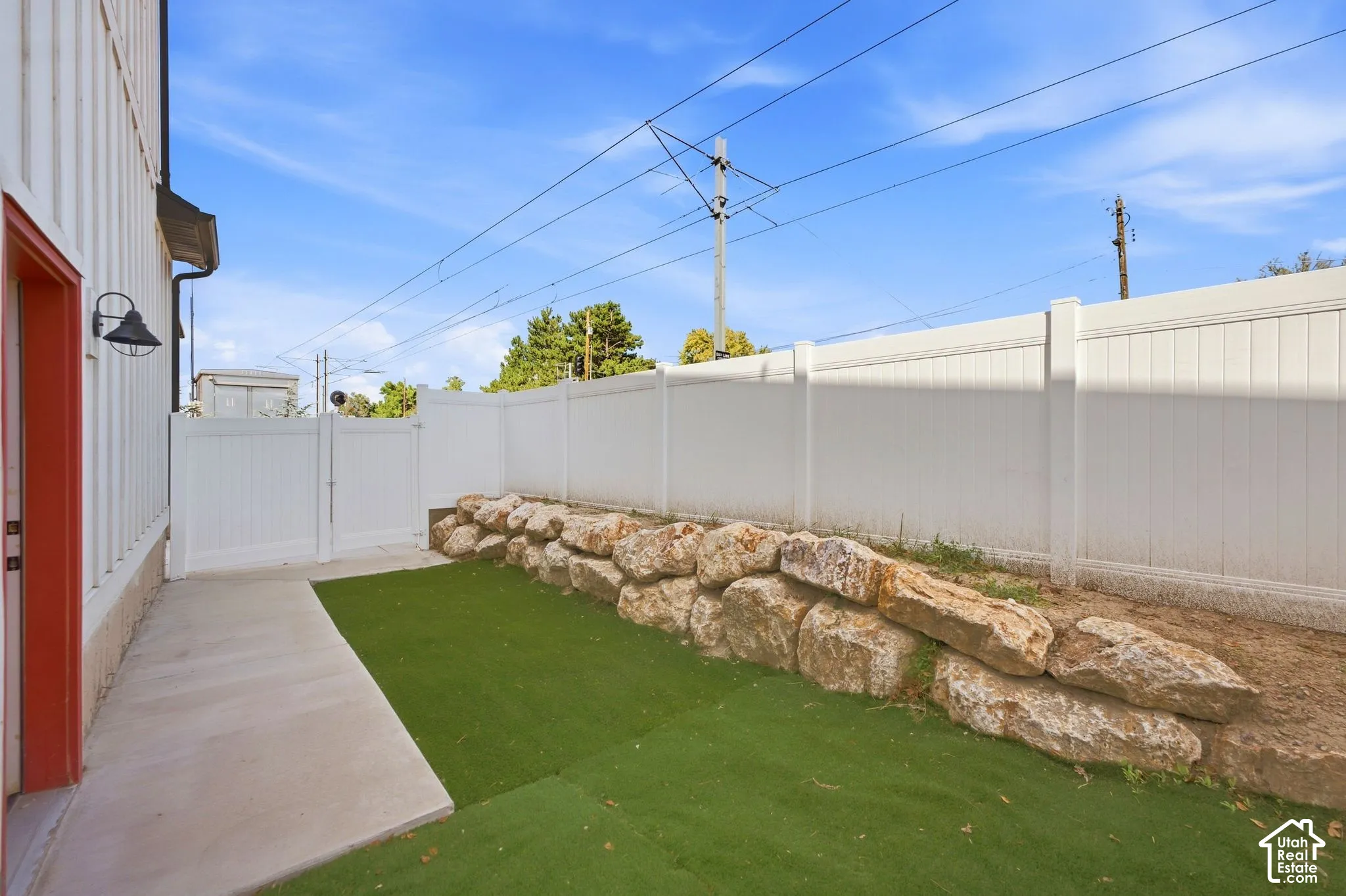 Private outdoor space with an artificial turf area, concrete patio, and a natural stone retaining wall
