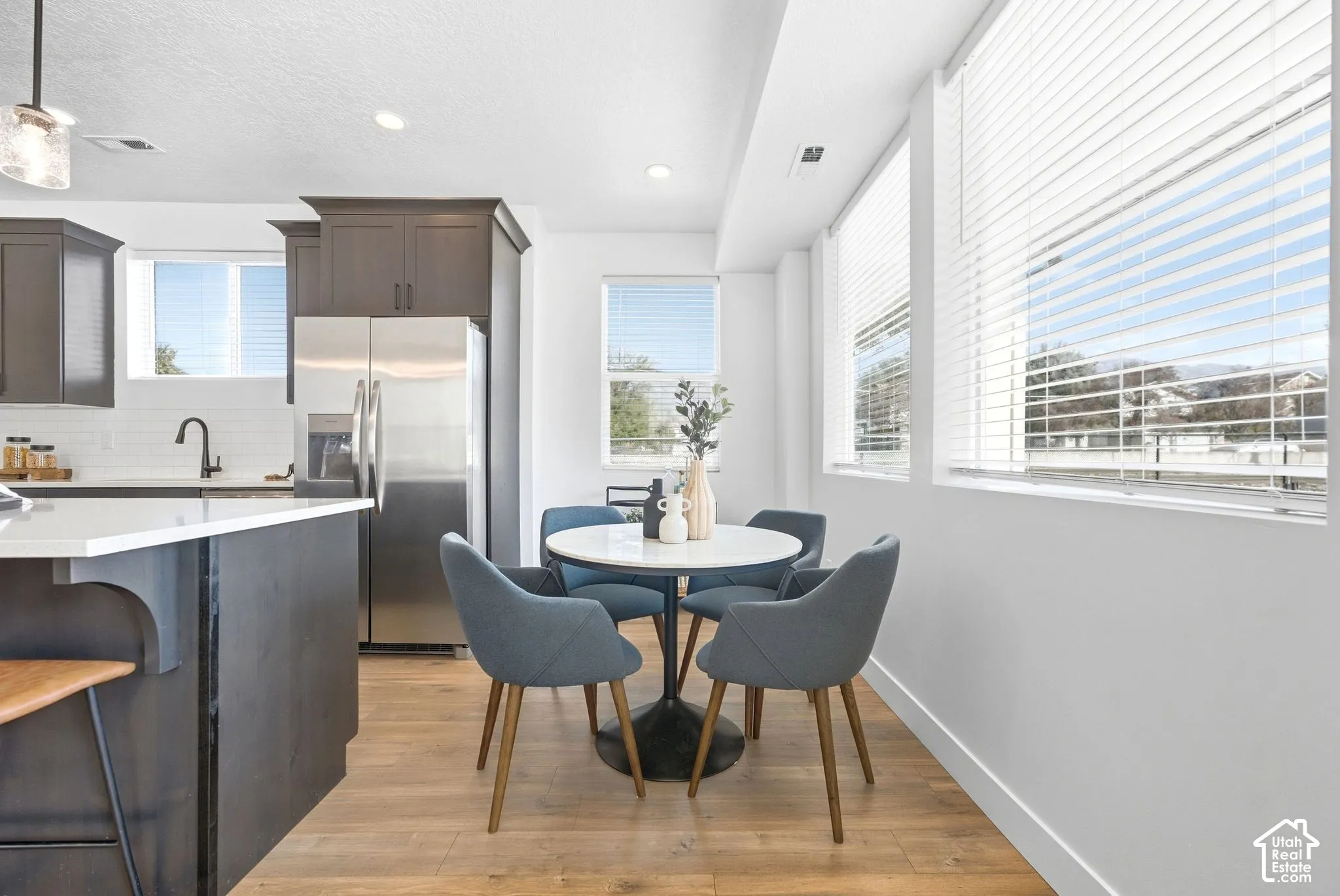 Modern kitchen featuring dark cabinetry, stainless steel appliances, a white tile backsplash, and light wood-finish flooring