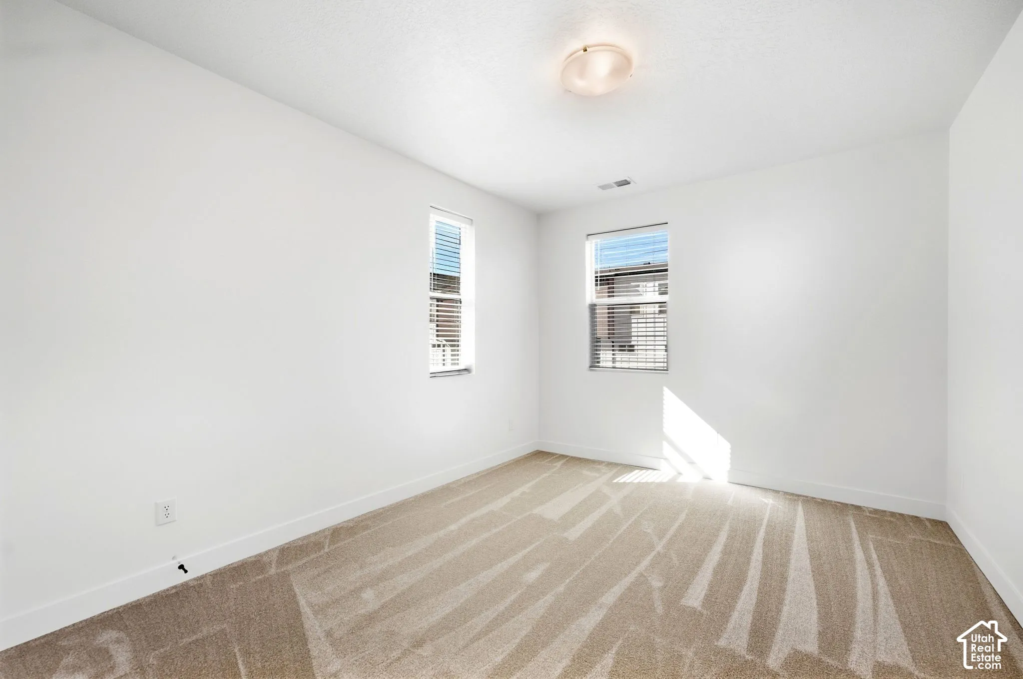 Bedroom 4 . Two windows with blinds, neutral carpet, and a flush mount ceiling light