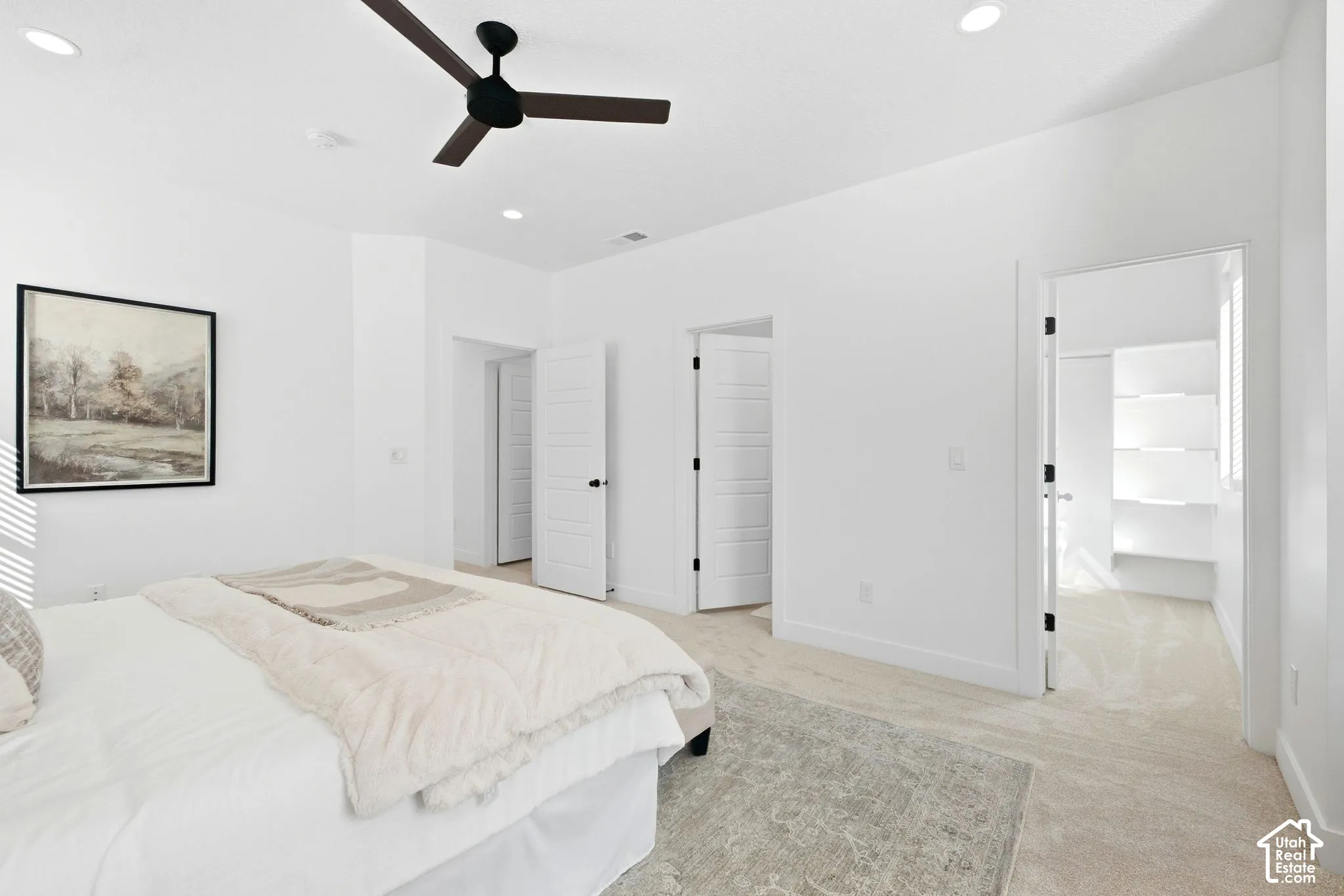 Primary bedroom. Neutral tone wall paint, recessed ceiling lighting, ceiling fan with dark blades, light-colored carpet flooring, and white paneled doors