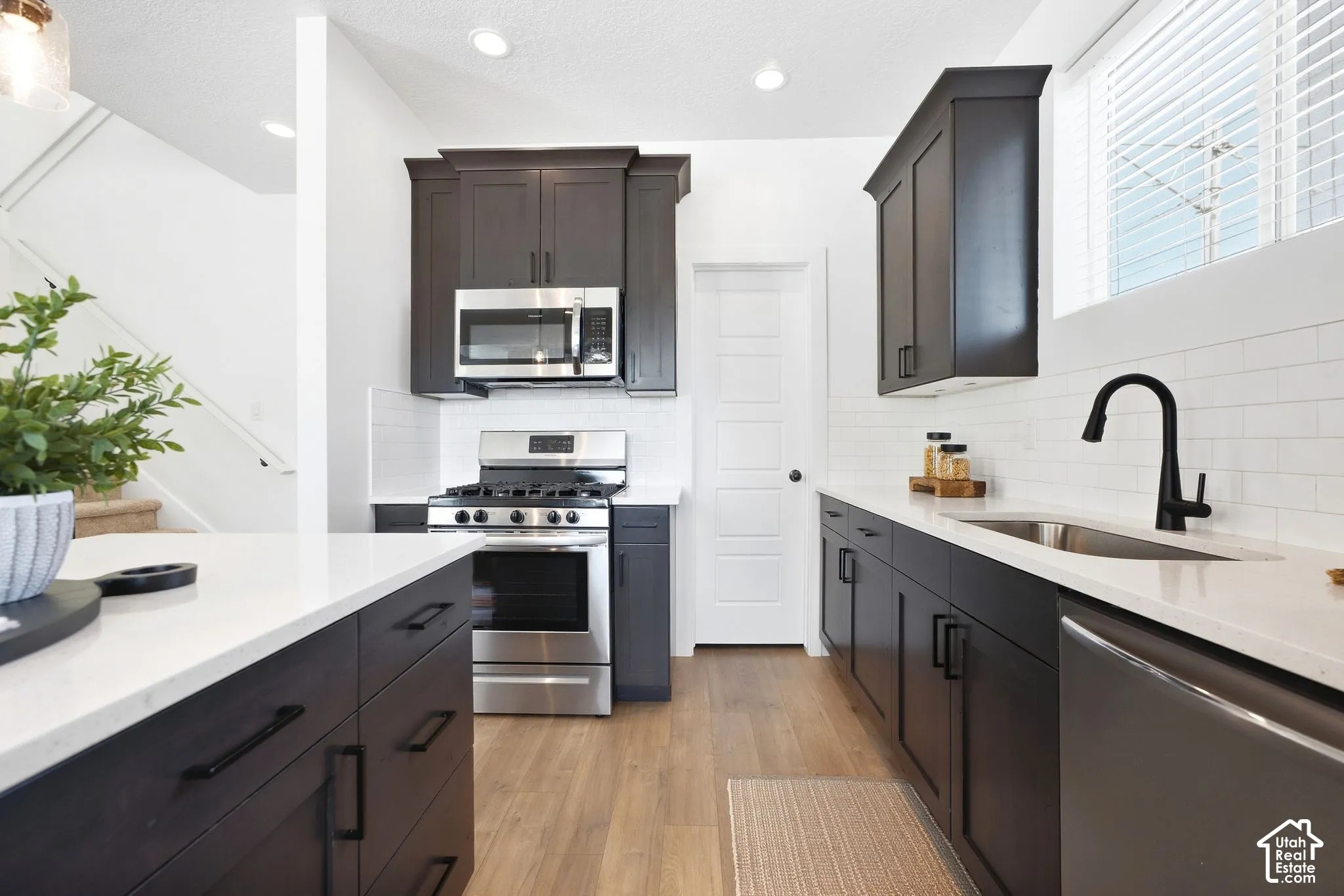 Kitchen featuring dark wood-finish cabinetry, light countertops, stainless steel appliances, a tile backsplash, and wood-finish flooring