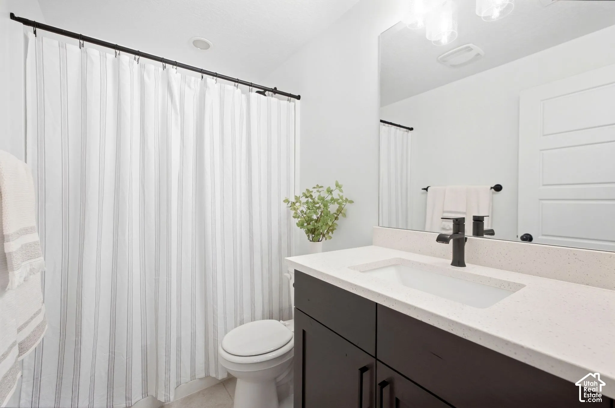 Bathroom featuring a single vanity with a solid surface countertop, an undermount sink, a matte black faucet, and a wall-mounted mirror