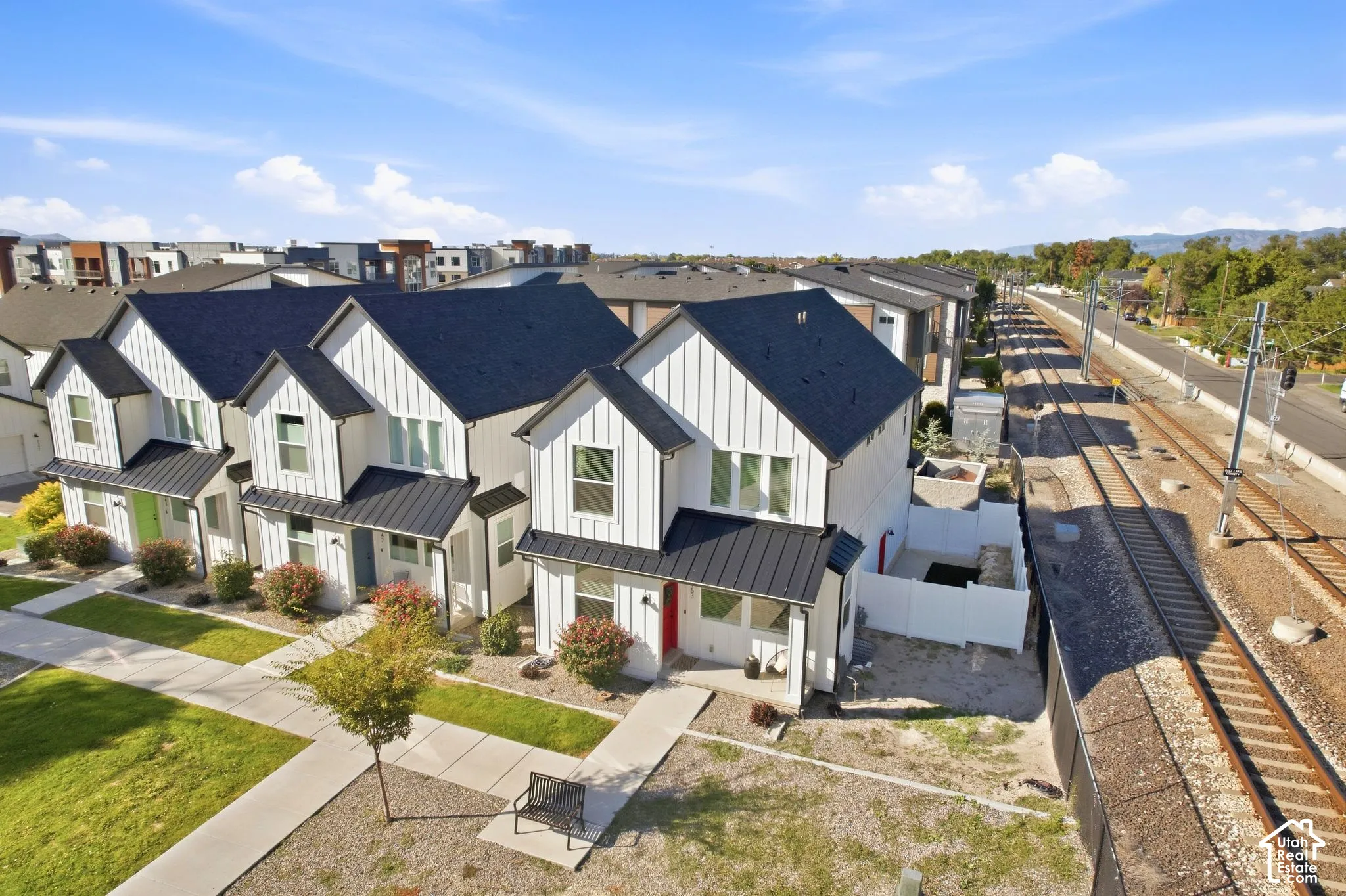 Modern farmhouse-style townhome featuring white vertical siding, black-pitched roofs, and a red front door