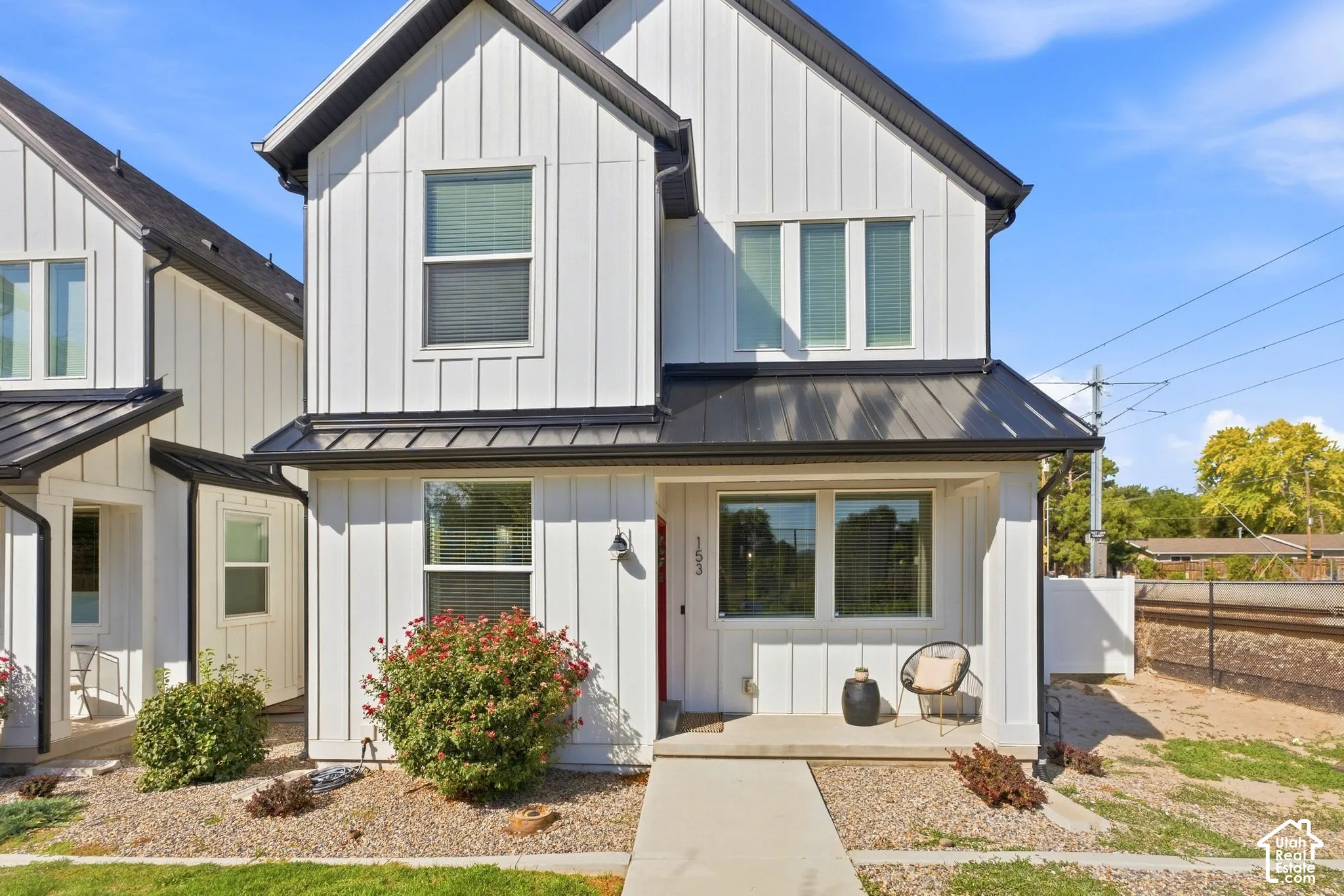 Board and batten siding, black metal roof accents, covered entry, concrete pathway, and established plantings