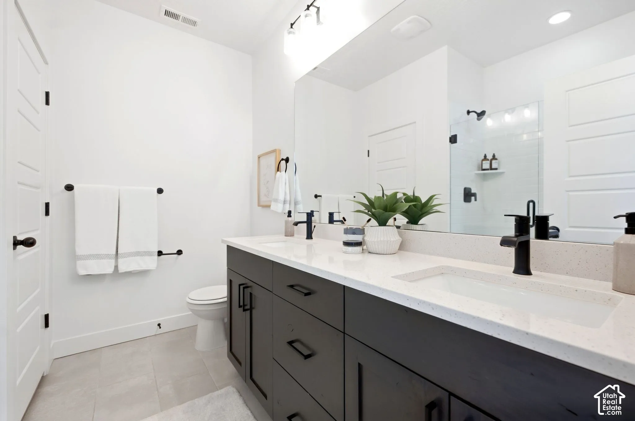 Primary bath. Spacious bathroom featuring a dual vanity with dark cabinetry, integrated sinks, a wide mirror, and a glass-enclosed shower with black fixtures
