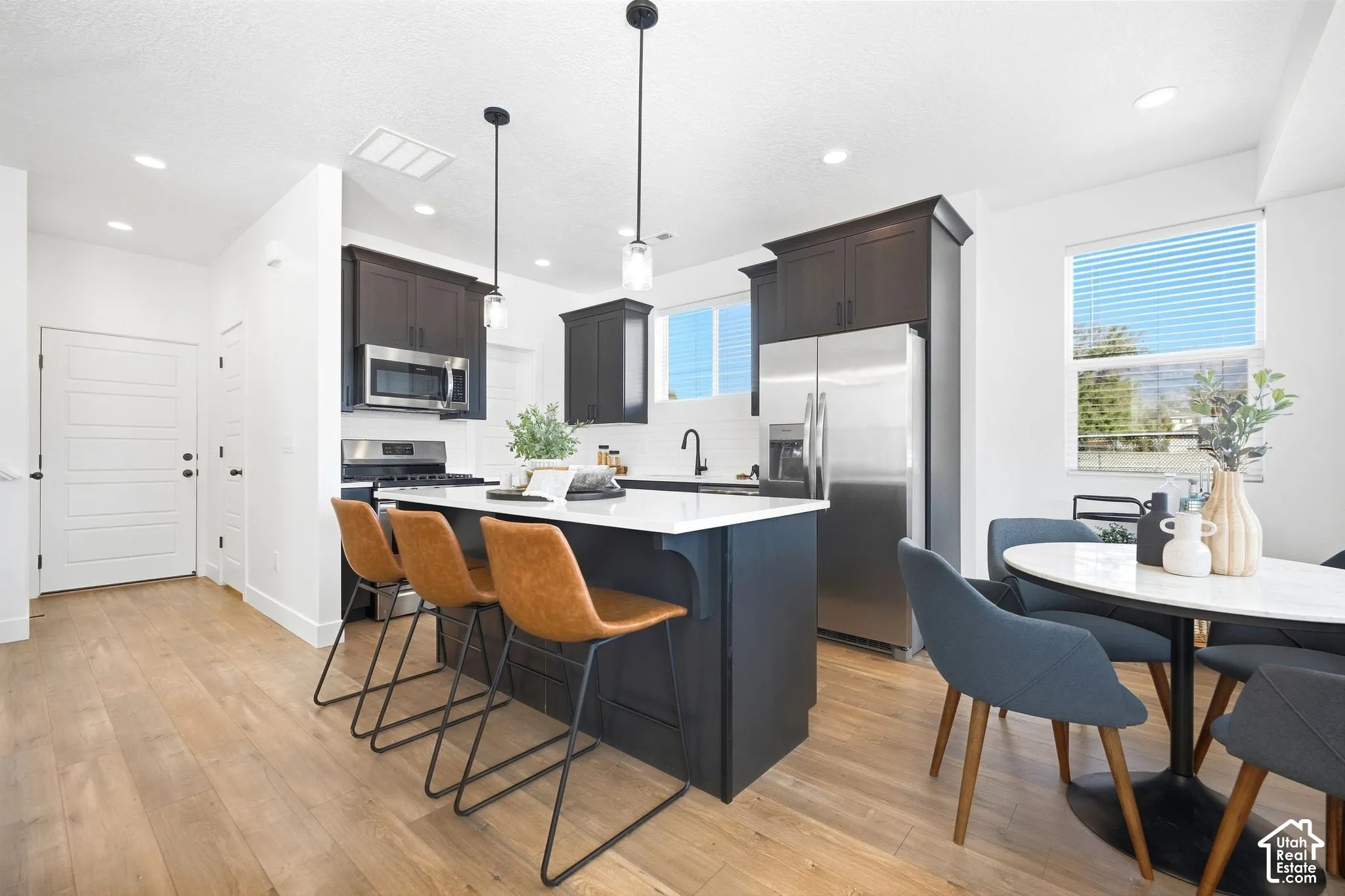 Open concept kitchen featuring an island with counter seating, dark wood cabinetry, stainless steel appliances, and wood-finish flooring