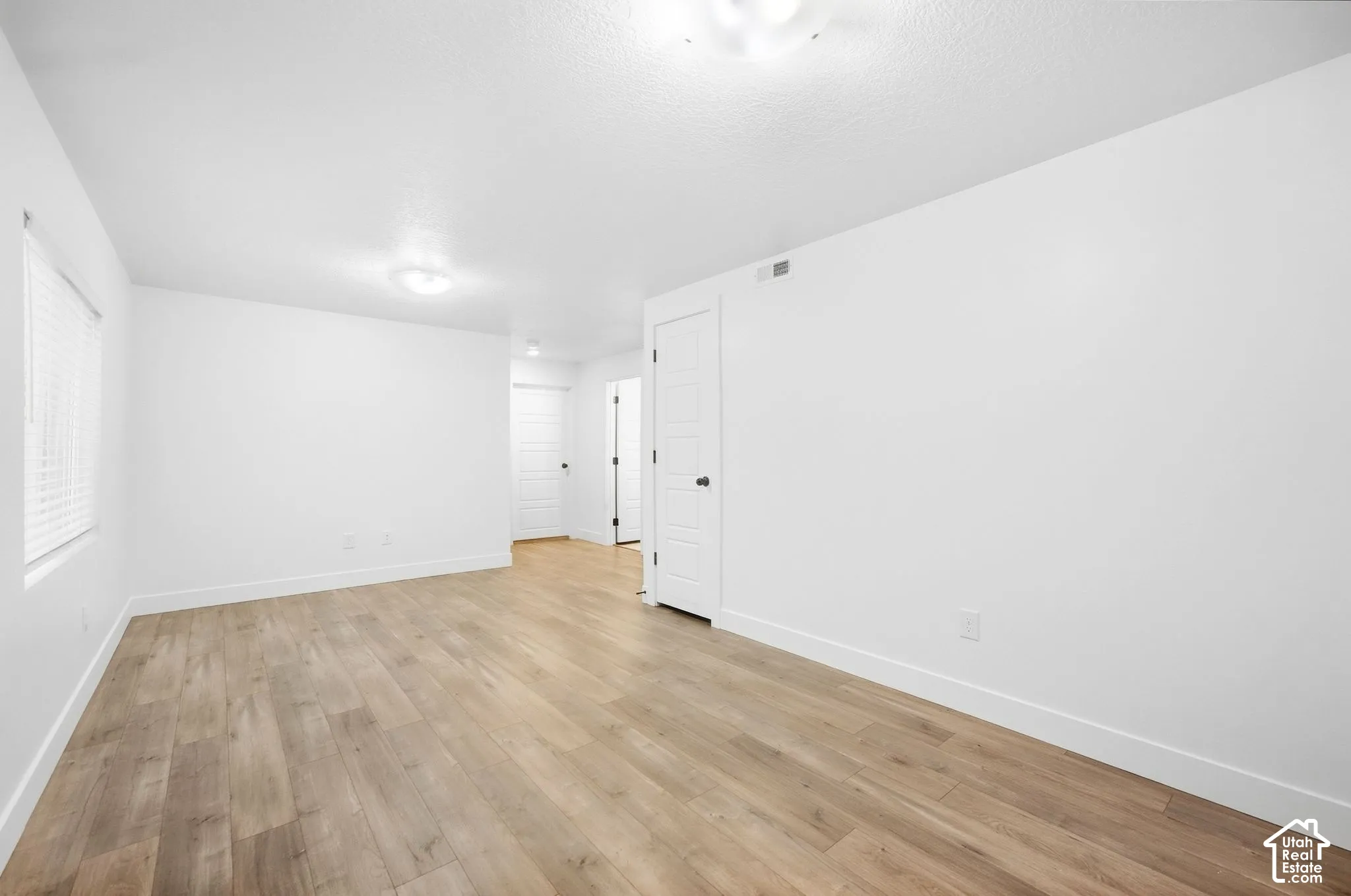 Expansive room featuring wood-finish flooring, white walls, and multiple solid panel doors