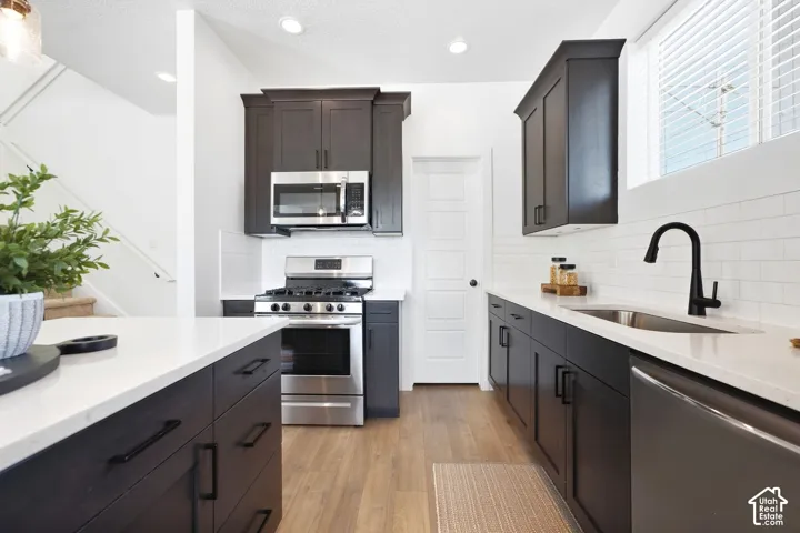 Kitchen featuring dark wood-finish cabinetry, light countertops, stainless steel appliances, a tile backsplash, and wood-finish flooring