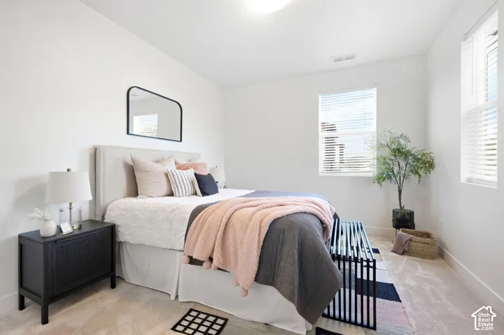 2nd bedroom.Bright bedroom featuring white walls, carpeted flooring, two windows with blinds, and an upholstered headboard