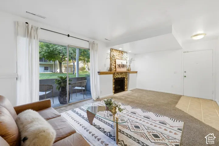Stone-clad fireplace with wood mantel, sliding glass door to patio, and carpeted flooring