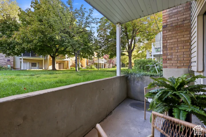Concrete patio with brick siding and a white column, overlooking a lawn with mature trees