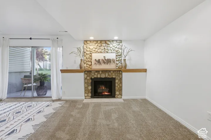Stone-clad fireplace with a wood mantle, recessed lighting, and sliding glass door leading to an outdoor patio
