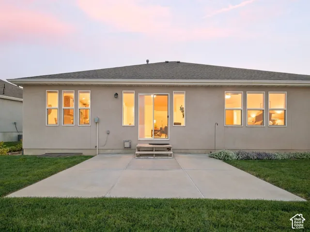 Expansive concrete patio with a manicured lawn, multiple large windows, and a sliding glass door