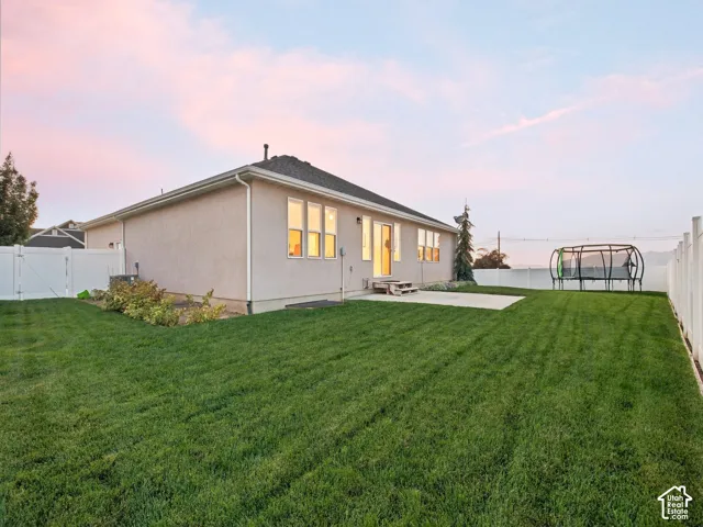 Expansive backyard featuring a manicured lawn, concrete patio, white vinyl fencing, and mature landscaping