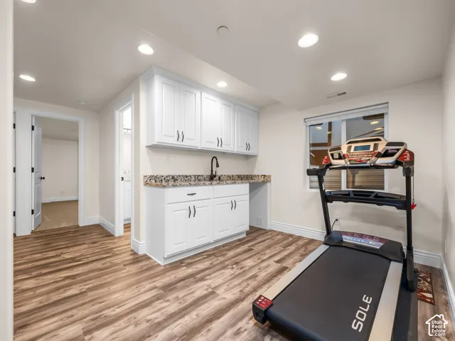 Wood-finish flooring with white cabinetry, granite-style countertop, and a matte black faucet