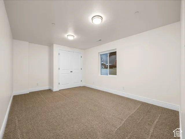 Neutral tone wall paint, brown carpet flooring, flush mount ceiling lighting, and a white window frame with a sliding pane