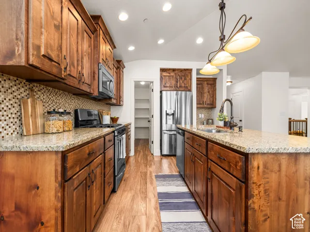 Kitchen featuring wood cabinetry, granite countertops, tile backsplash, stainless steel appliances, and wood-finish flooring