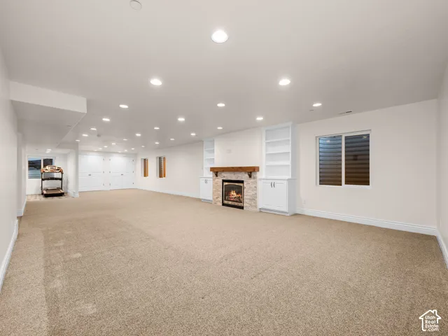 Spacious room featuring carpeting, recessed lighting, a fireplace with a wood mantle, built-in shelving, and a window